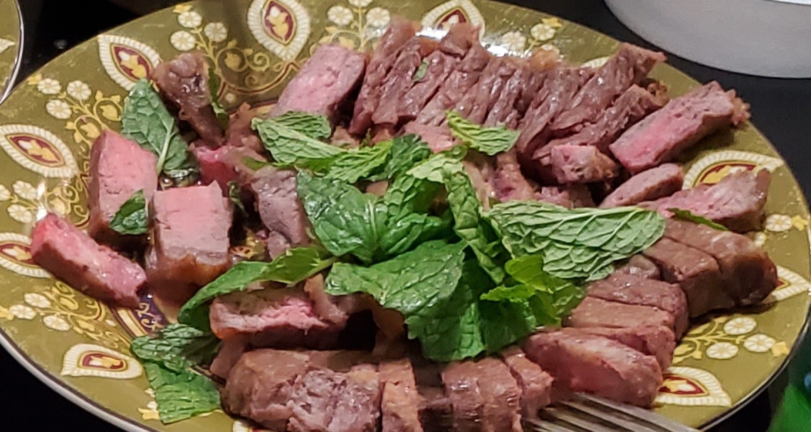sliced steak garnished with fresh mint leaves